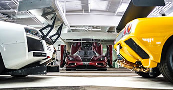 Three high-performance sports cars are showcased in a garage, with a striking red car prominently positioned in the center.